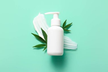 Bir şişe kenevir kozmetik ürünü ve turkuaz arka planda yapraklar