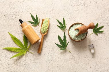 Bir şişe kenevir kozmetik yağı, deniz tuzu ve beyaz arka planda yapraklar.