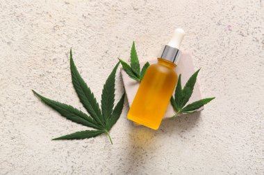 Kenevir kozmetik yağı şişesiyle dekoratif podyum ve beyaz arka planda yapraklar