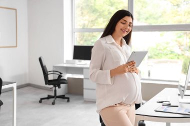 Ofiste tablet bilgisayarla çalışan hamile bir iş kadını.