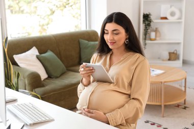 Ofiste tablet bilgisayarla çalışan hamile bir iş kadını.