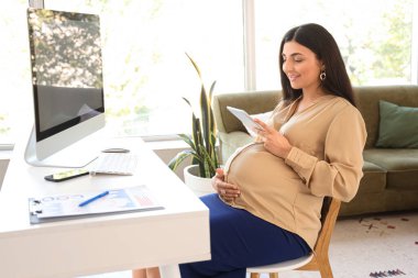 Ofiste tablet bilgisayarla çalışan hamile bir iş kadını.