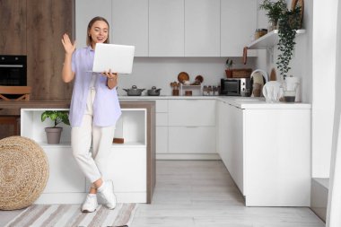 Dizüstü bilgisayarı olan genç bir kadın mutfakta sohbet ediyor.