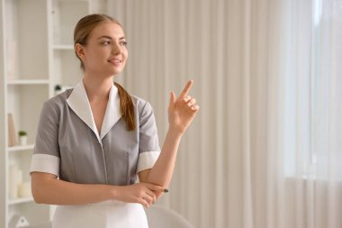 Genç hizmetçi odadaki bir şeyi işaret ediyor.