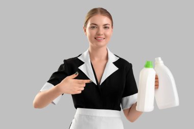 Genç hizmetçi arka planda deterjan şişelerine bakıyor.