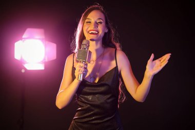 Koyu arkaplanda parlayan lamba ve mikrofonlu kadın şarkıcı.