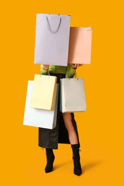 Sarı arka planda alışveriş torbaları olan şık genç bir kadın. Kara Cuma İndirimi