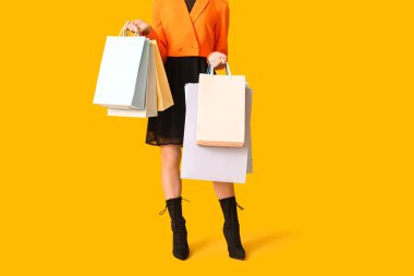 Sarı arka planda alışveriş torbaları olan genç bir kadın. Kara Cuma indirimi