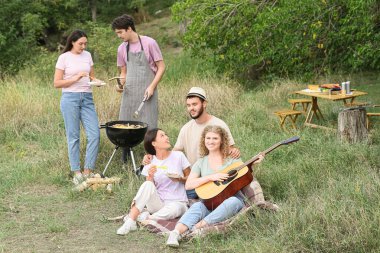 Barbekü partisinde arkadaşlarıyla gitar çalan genç bir kadın.