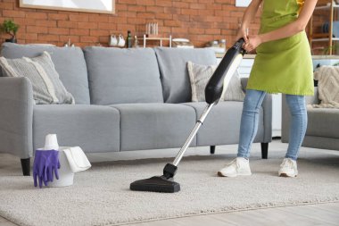 Evde elektrikli süpürgeyle halı temizleyen genç bir kadın, yakın plan.