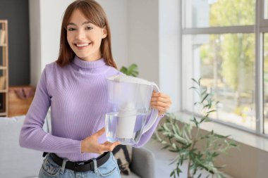 Evde su filtresi taşıyan genç bir kadın var.