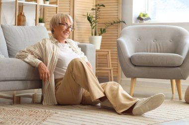 Evdeki kanepenin yanında oturan yaşlı kadın.