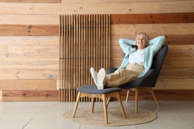 Yaşlı kadın evdeki taburede ayaklarıyla koltukta dinleniyor.