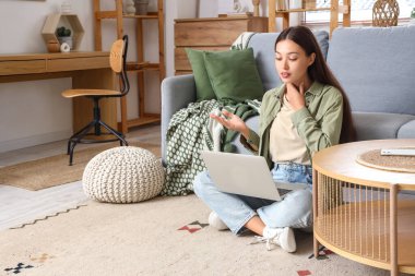 Tiroid bezi sorunu olan genç bir Asyalı kadın ve evde dizüstü bilgisayarla görüntülü sohbet.