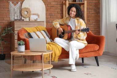 Gitarlı genç Afro-Amerikalı kadın evde sohbet ediyor.