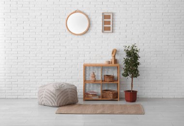 Raflama ünitesi, puf, dekoratif ağaç ve ayna beyaz tuğla duvarda.