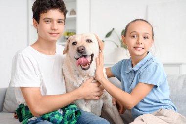 Mutlu kız ve erkek kardeş ve şirin Labrador köpeği evdeki kanepede oturuyor.