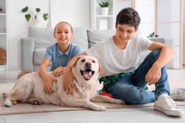 Mutlu kız ve erkek kardeş ve şirin Labrador köpeği evde yerde oturuyor.