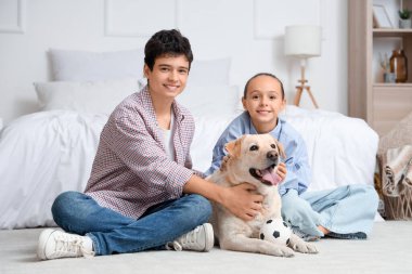 Mutlu kız ve erkek kardeş ve şirin Labrador köpeği evdeki yatak odasında yerde oturuyor.