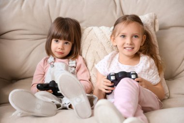 Mutlu kız kardeşler evdeki kanepede oyun oynuyorlar.