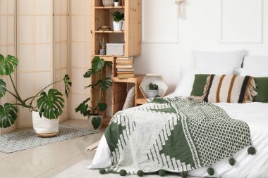 Şık bir yatak odası, raf ünitesi, farklı bitkiler ve büyük bir yatak.