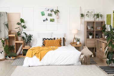 Farklı ev çiçekleri, raf üniteleri ve büyük yataklı şık bir yatak odası.