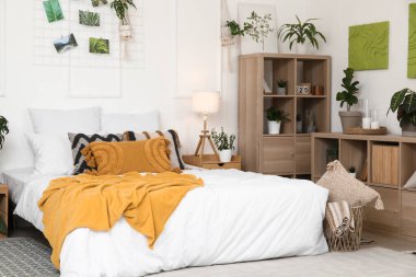 Farklı ev çiçekleri, raf üniteleri ve büyük yataklı şık bir yatak odası.