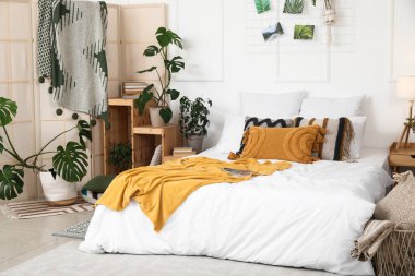 Farklı ev çiçekleri, kitaplık ve büyük yataklı şık bir yatak odası.