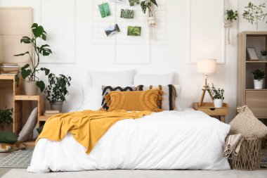 Farklı ev çiçekleri, kitaplık ve büyük yataklı şık bir yatak odası.