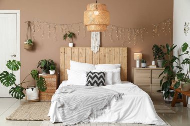 Şık bir yatak odası, farklı bitkiler, parlak bir çelenk ve büyük bir yatak.