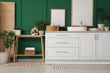 Ahşap bank, çekmece sandığı ve yeşil duvarın yanındaki katlı ekran.