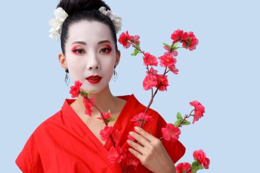 Açık arkaplanda çiçek açan sakura dalına sahip güzel genç geyşa.