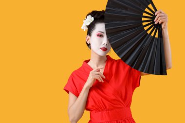 Beautiful young geisha with fan on yellow background clipart