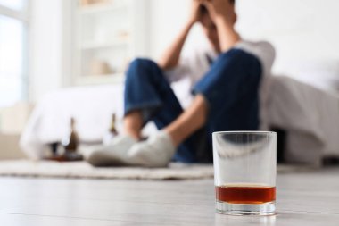 Sarhoş bir gencin yatak odasında yerde bir bardak viski. Alkolizm kavramı