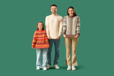 Yeşil arka planda kazaklı kızları olan mutlu bir aile.