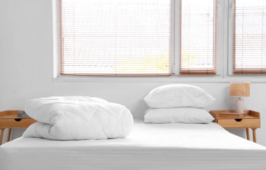 Yatak odasının penceresinin yanındaki yatakta yastıklar ve katlanmış beyaz battaniye.