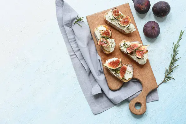 Lezzetli incir bruschetta tahtası ricotta peyniri ve açık mavi arka planda biberiye.