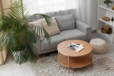 Oturma odasının iç tarafındaki pencere kenarındaki masa, kanepe ve çiçek.