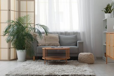 Oturma odasının içinde kanepe, katlanan ekran ve pencerenin yanındaki masa.