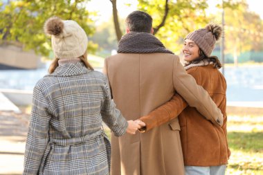 Erkek ve iki güzel kadın, sonbahar parkında yürürken el ele tutuşuyorlar. Poliyamory konsepti