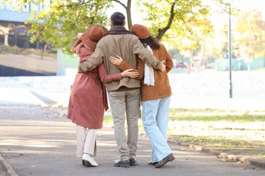 Sonbahar parkında sarılan bir adam ve iki kadın. Poliyamory konsepti