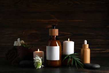 Kozmetik ürünleri, spa aksesuarları, yanan mumlar ve koyu ahşap arka planda çiçekler.