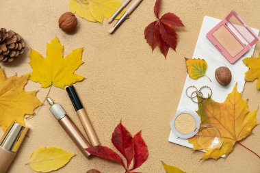 Renk arkaplanındaki kozmetik ürünler, aksesuarlar ve sonbahar yapraklarından oluşan çerçeve