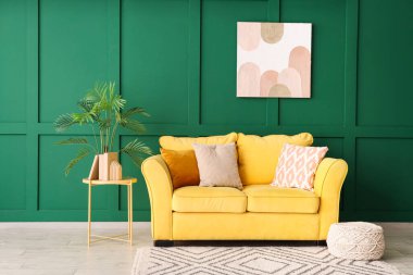 Yeşil duvarın yanında rahat sarı kanepesi ve sehpası olan şık bir oda.