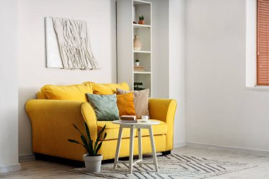 Rahat sarı kanepesi, sehpası ve raf ünitesi olan şık bir oda.