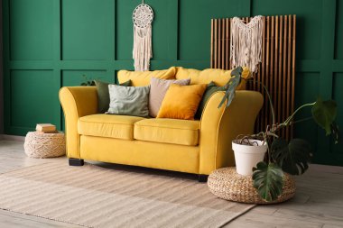 Yeşil duvarın yanında rahat sarı kanepesi ve çiçekleri olan şık bir oda.