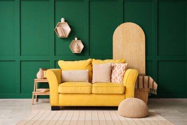 Yeşil duvarın yanında rahat sarı kanepesi ve sehpası olan şık bir oda.