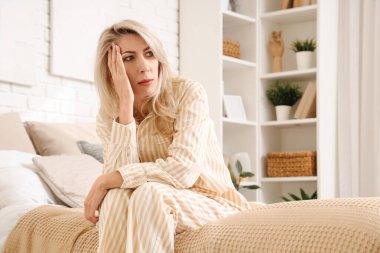 Yatak odasında menopoz geçiren, baş ağrısı olan olgun bir kadın.