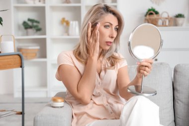 Evde aynaya bakan üzgün olgun bir kadın. Menopoz kavramı