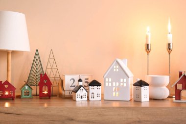 Bej duvarın yanındaki rafta Noel dekoru olan ev şekilli mum tutacakları.